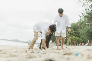Asian family collecting plastic waste on the beach.  young people friends picking up trash and...