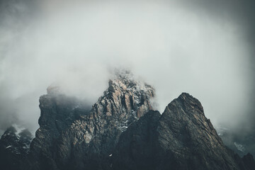 Dark atmospheric surreal landscape with dark rocky mountain top in low clouds in gray cloudy sky....