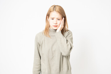 歯が痛くて頬に手を当てるセーターを着た若い女性