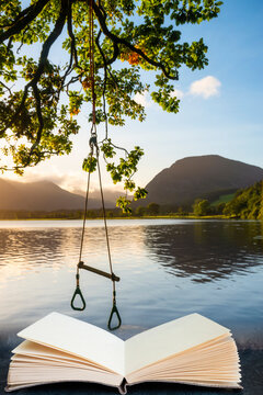 Quintessential Beautiful English Summer Landscape Image Of Child's Rope Swing Over Calm Lake In Lake District Coming Out Of Pages In Reading Book