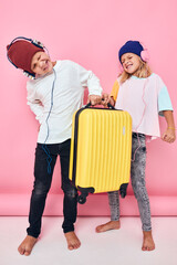 funny little boy and girl with a yellow suitcase in his hands studio posing