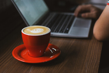 Shot of a man working on his laptop with a coffee cup on table.