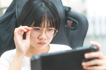 Young adult asian gamer woman wear eyeglasses play a handheld online game.