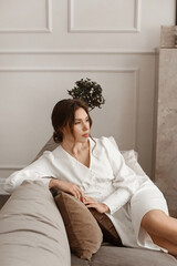 A fashionable brown-haired young woman in an elegant white dress poses at the vintage living-room