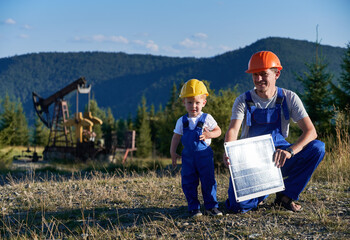 Portrait of professional Caucasian mechanic with solar panel learning capable boy derrick maintenance, father and son dressed in blue uniform looking at camera during daytime at petroleum station