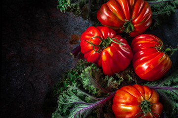 Flat lay of big fresh ripe tomatoes with kale leaves and wooden cutting board on the rustic dark blue background