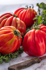 Fresh furrowed organic tomatoes from farmers market on the marble stove with green curly kale leaves. Close up and soft focus.