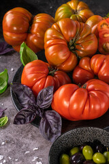 Whole and sliced organic tomatoes Raf Coeur De Boeuf. Raw fresh tomatos with sea salt and basil and olives in plates. Side view with soft focus.