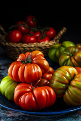 Raw fresh tomatoes on dark blue plate. Group of lined creasy organic Raf tomatos. Low key side view photo with soft focus.