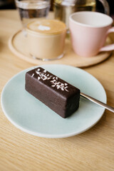 Tasty vegan row chocolate dessert on plate on background of coffee and tea mugs. Сozy coffee shop. 