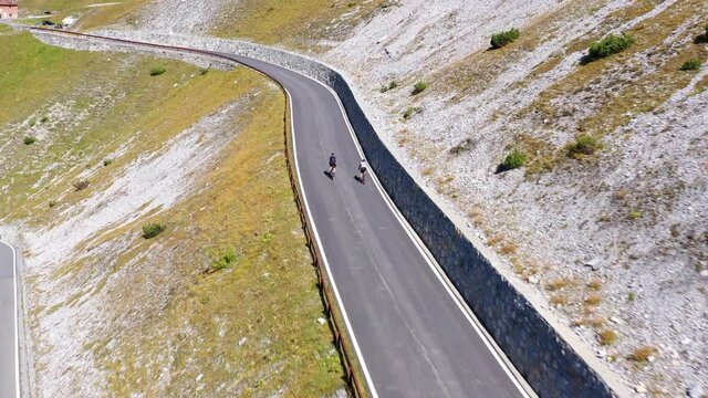 Aerial drone footage of cyclists biking along the famous Stelvio mountain pass in the alps in Italy on a sunny summer day. 