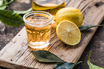 Traditional homemade lemon liqueur limoncello and fresh citrus on a wooden table.