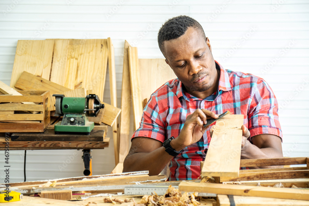 Wall mural young carpenter african american man looking and choosing wood and using sandpaper to rub wooden pla