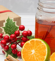 Black tea in a glass jar, lemon, cinnamon and a gift box on a white wooden background. Christmas and New Year concept