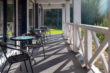 Close up of a table and chairs standing at an open area of house terrace in sunny day, close to the large windows