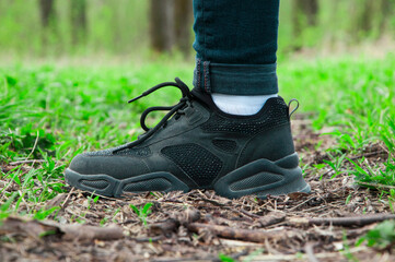 sneakers on the path. girl stands with her foot in the woods. illustration of travel. black shoes on a natural background. hiking concept