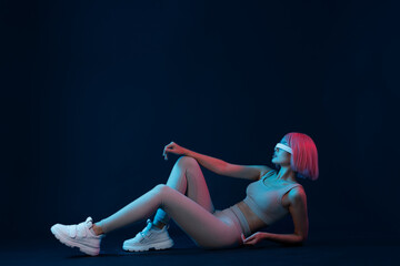 Obraz premium Woman in futuristic costume. Female in modern VR glasses interacting with network while having virtual reality experience. Augmented reality game, future technology, AI concept. VR. Neon blue light.