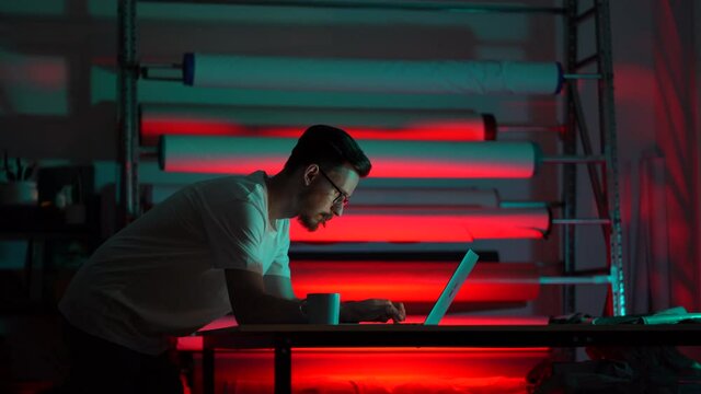 Creative man stylist or fashion designer work on laptop in atelier. Male tailor use computer for creating patterns of clothes collection in studio. Self-employed dressmaker businessman in office