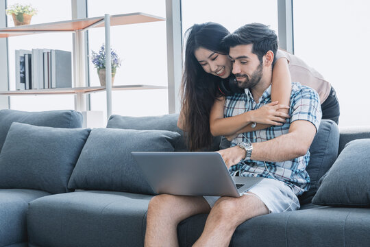 Smiling Woman Hugging Her Husband On The Couch From Behind In The Living Room.