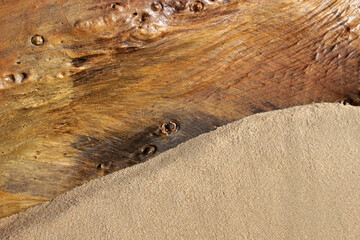 Background of the contrast between where clean golden beach sand and a large piece of driftwood meet
