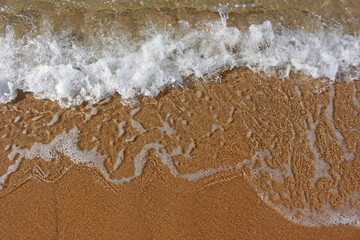 Above view pattern of a small clean ocean wave washing onto golden beach sand. 