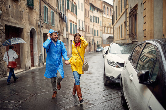 A young couple in raincoats is holding hands and walking the city during a rain. Walk, rain, city, relationship
