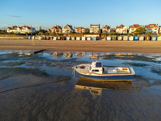 Boat in sea near Southend beach at low tide near Thorpe bay during sunset at a sunny autumn day. reflection on the boat and beach huts. Drone aerial view