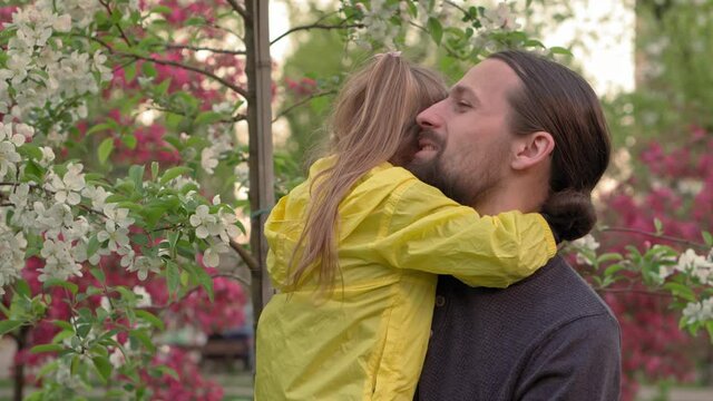 people in park. dad hold baby daughter girl in arms near blossoming apple tree and sniffing flowers. parents and fun children walking outdoors in open air. Fathers day, childhood, parenthood concept