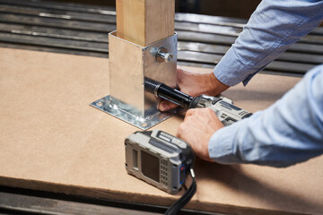 male hands screw the nut to furniture fittings with an automatic wrench with battery