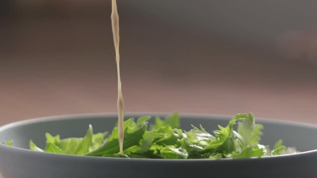 Slow motion pour dressing on green frisee lettuce in blue bowl closeup