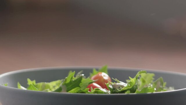 Slow motion cherry tomatoes fall on green frisee lettuce in blue bowl closeup