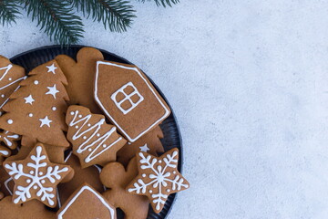 Christmas gingerbread cookies, on a dark plate, a fir branch on a light background. New Year. Place for your text. Flat lay.
