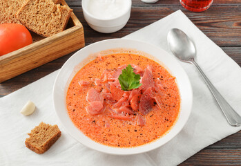 borscht with sour cream and parsley in a white plate on a dark wooden background, spoon, parsley, bread, napkin