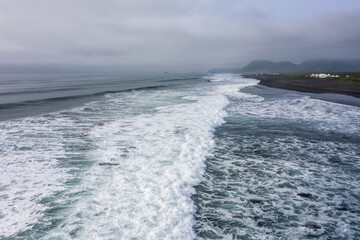 Turquoise waves with white foam and black sand  in the Pacific Ocean, drone bird's eye view