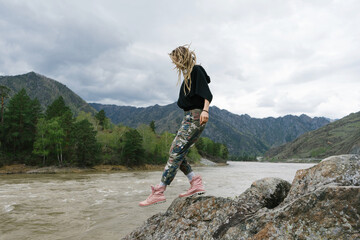Woman wearing dreadlocks walking on rocky beach of mountain river