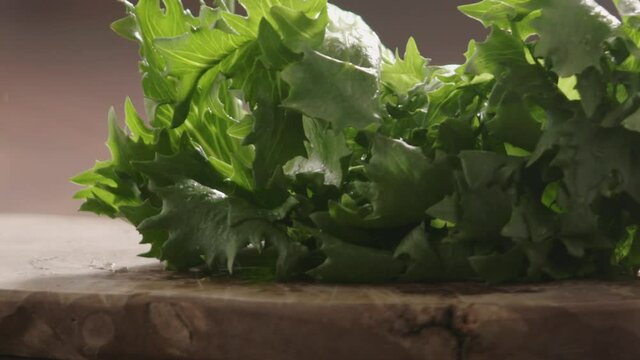 Slow motion washed lettuce fall on olive wood baord closeup