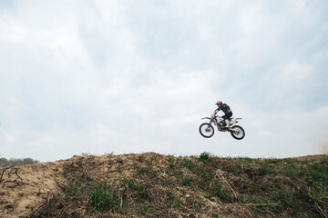 Naklejka premium Motorcyclist jumping and riding on rear wheel at enduro motocross training ground