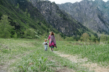 Young mother carrying  child on her back. Woman walking in the mountains with son