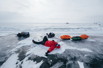 Tourist Man Lying and relaxing on frozen ice of Lake Baikal. Winter trekking