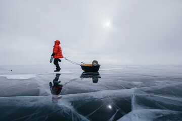 Naklejka premium Tourist walking with sleigh dragging on the frozen ice of Lake Baikal. Winter trekking