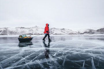 Tourist walking with sleigh dragging on the frozen ice of Lake Baikal. Winter trekking