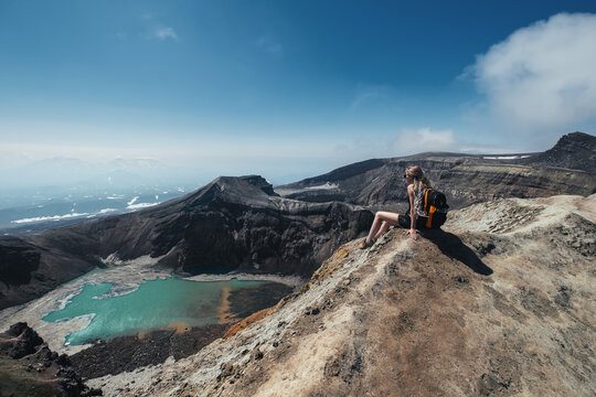 Woman with backpack sitting  on the mountain top above crater and lake of Gorely volcano, Kamchatka