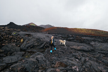 Traveler female walking with her dog on the frozen lava of volcano. Hiking in the mountains of...