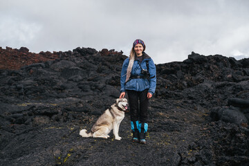Traveler female walking with her dog on the frozen lava of volcano. Hiking in the mountains of Kamchatka