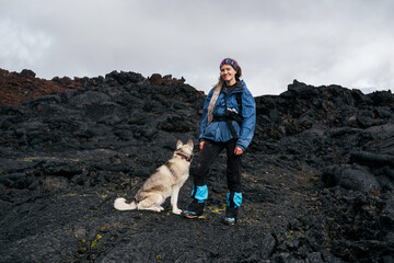 Traveler female walking with her dog on the frozen lava of volcano. Hiking in the mountains of...