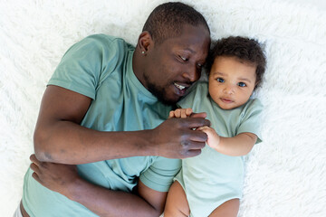happy smiling African american dad with baby son on bed at home cuddle, happy family, father's day