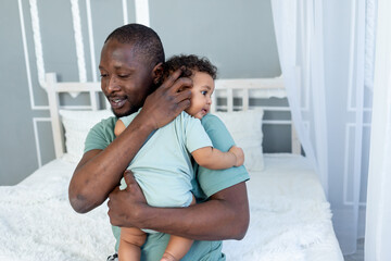 African-American dad hugs baby son holding him at home, happy family, Father's Day