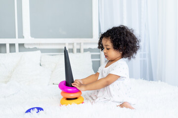 african American baby girl plays and collects a colorful pyramid at home on the bed