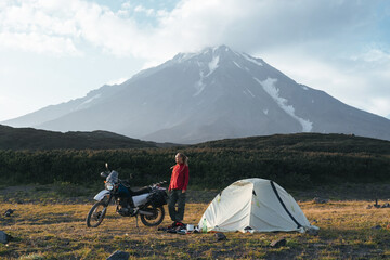 woman traveling on a motorcycle standing near a tent under the active volcano, Kamchatka