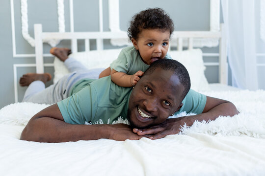 african-American dad plays rattle with baby son at home on bed in bedroom, father's love